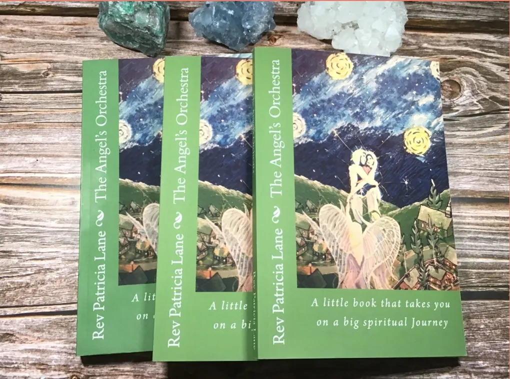 The Angel's Orchestra by Rev Patricia Lane — three copies of the book on a rustic wood table with crystals