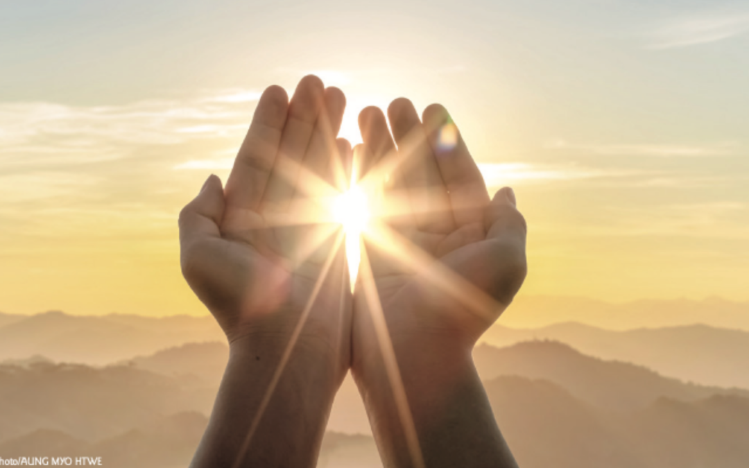 Cupped hands raised to the sunrise over mountains