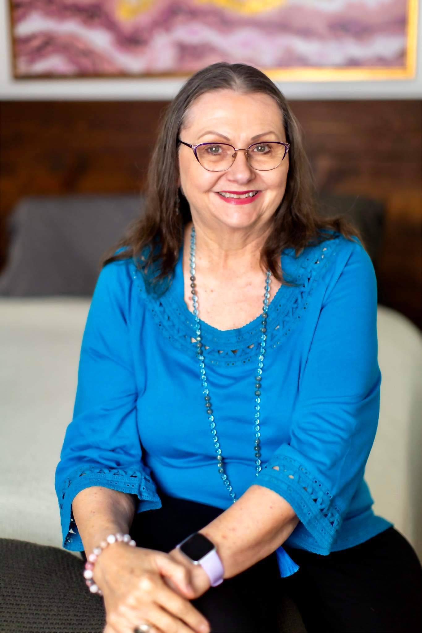 Patricia LaDale Lane smiling, seated, wearing a blue lace-trimmed top and beaded necklace