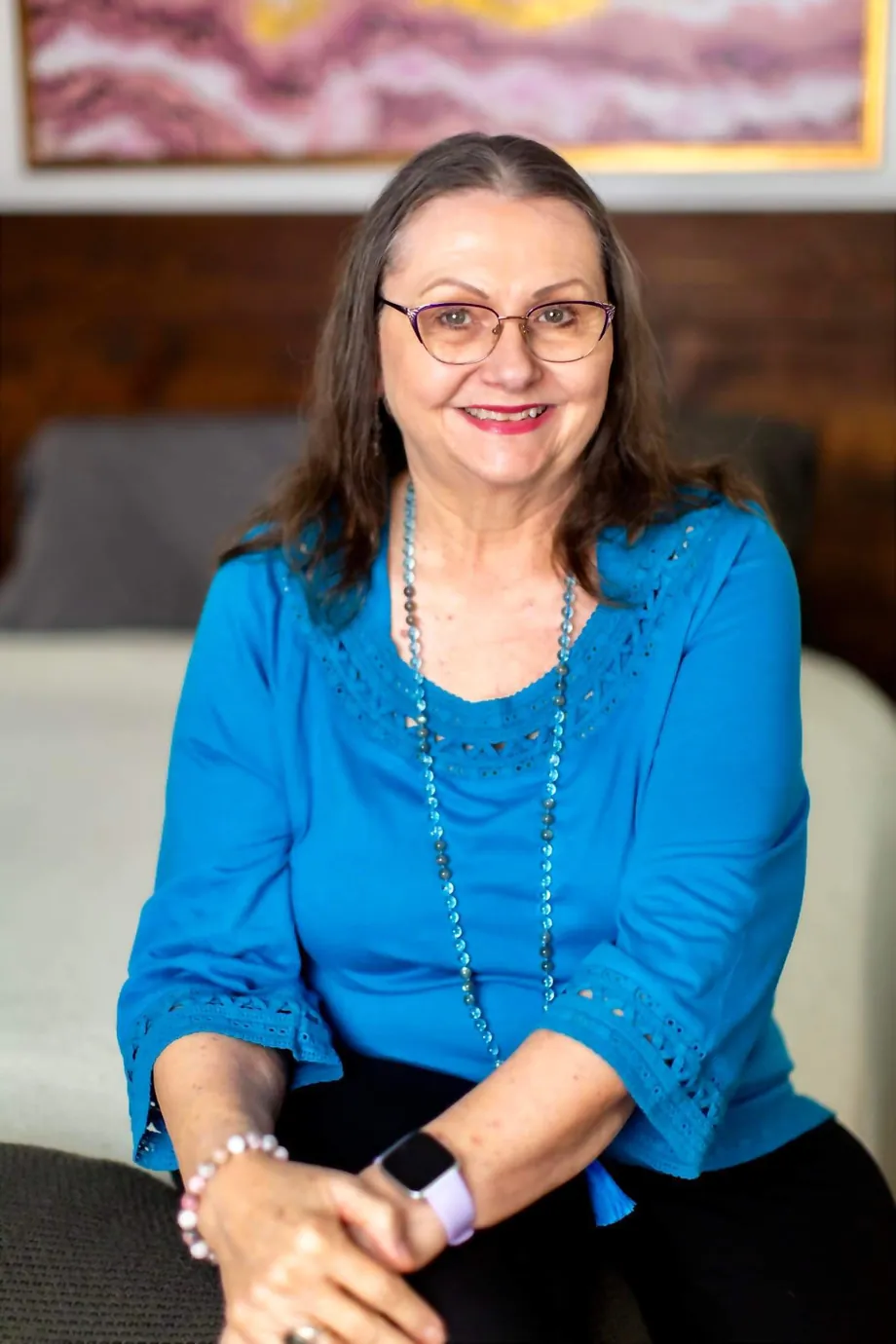 Patricia LaDale Lane smiling, seated, wearing a blue lace-trimmed top and beaded necklace